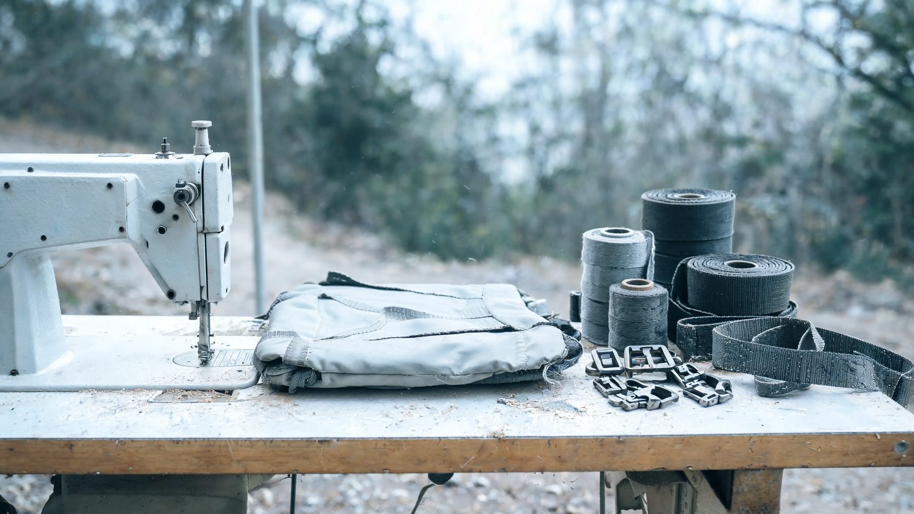 Workshop table with a half-stitched pack panel, webbing spools and buckles